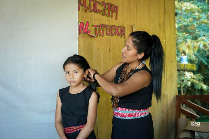 Mujer peina a una niña durante una conmemoración comunitaria